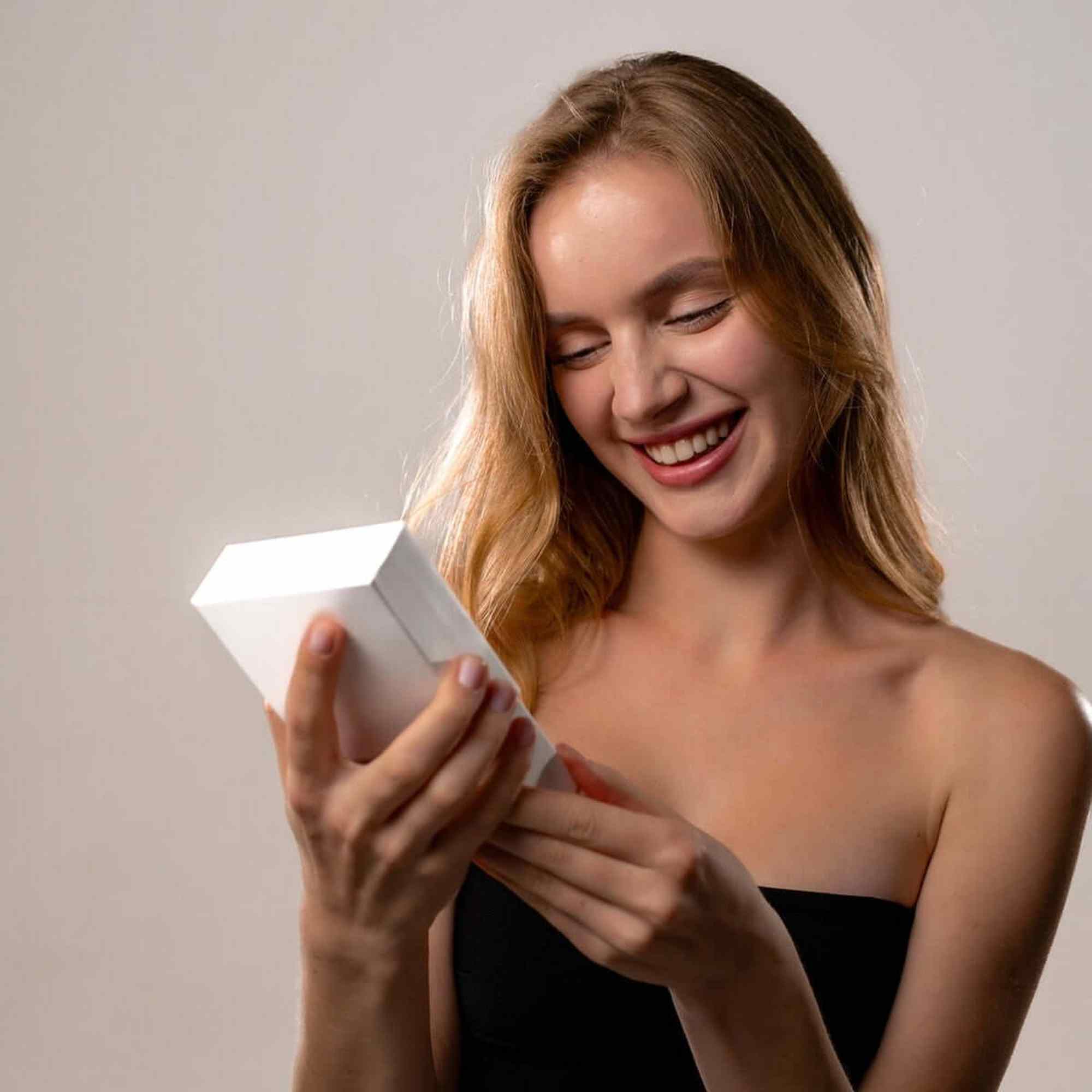 Smiling woman holding a white gift box, excited about the Love Photo Necklace by Brother & Sisters.