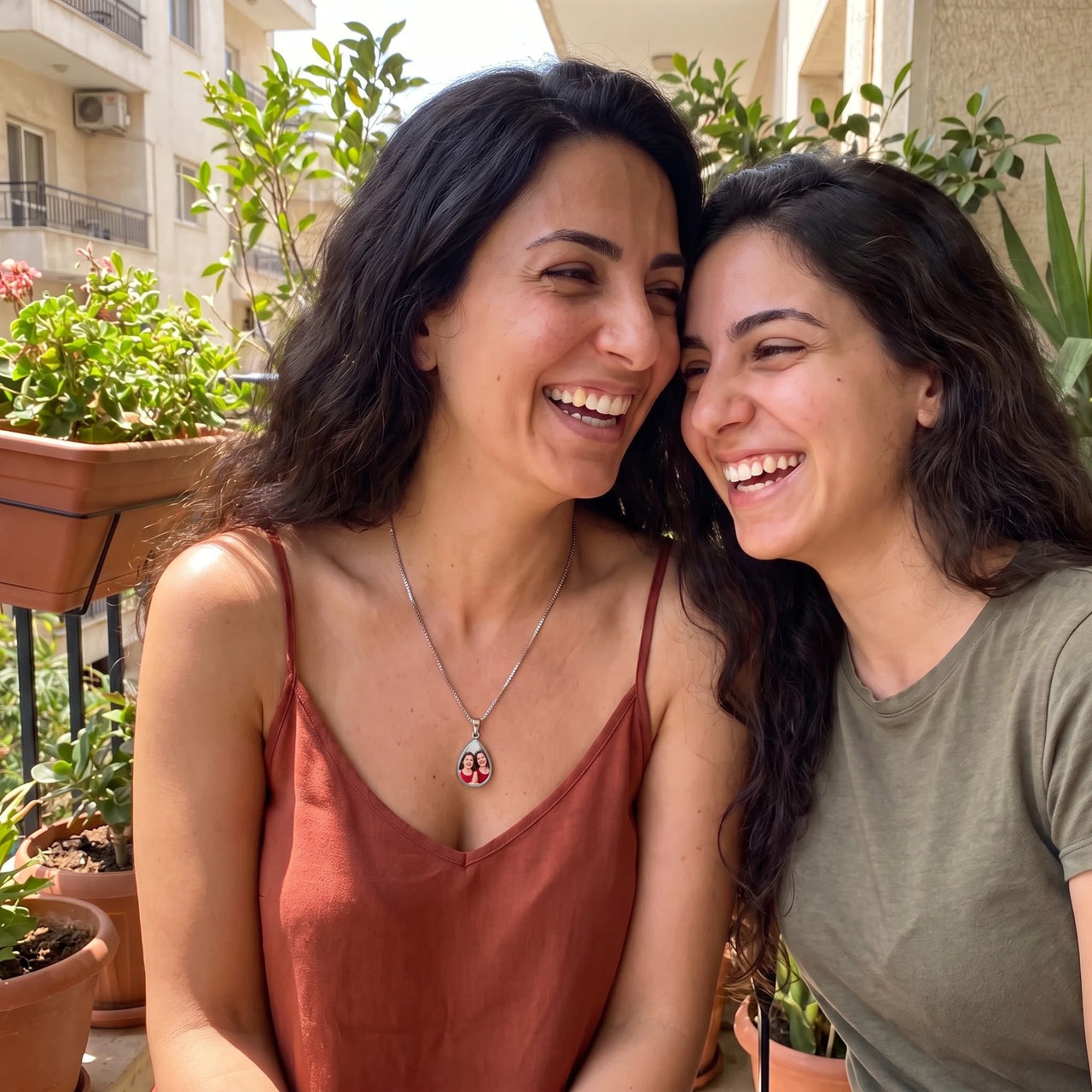 Two women laughing together on a balcony, one wearing the silver secret drop photo necklace | SKU: TPH-DRPN-SILVER