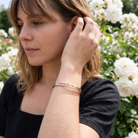 Thumbnail for Woman gently touching her Travel To Feel Alive bracelet in rose gold | SKU: ttfa-rg
