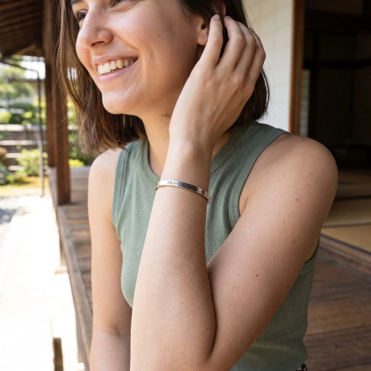 Woman gently touching her Travel To Feel Alive bracelet in silver | SKU: ttfa-wg